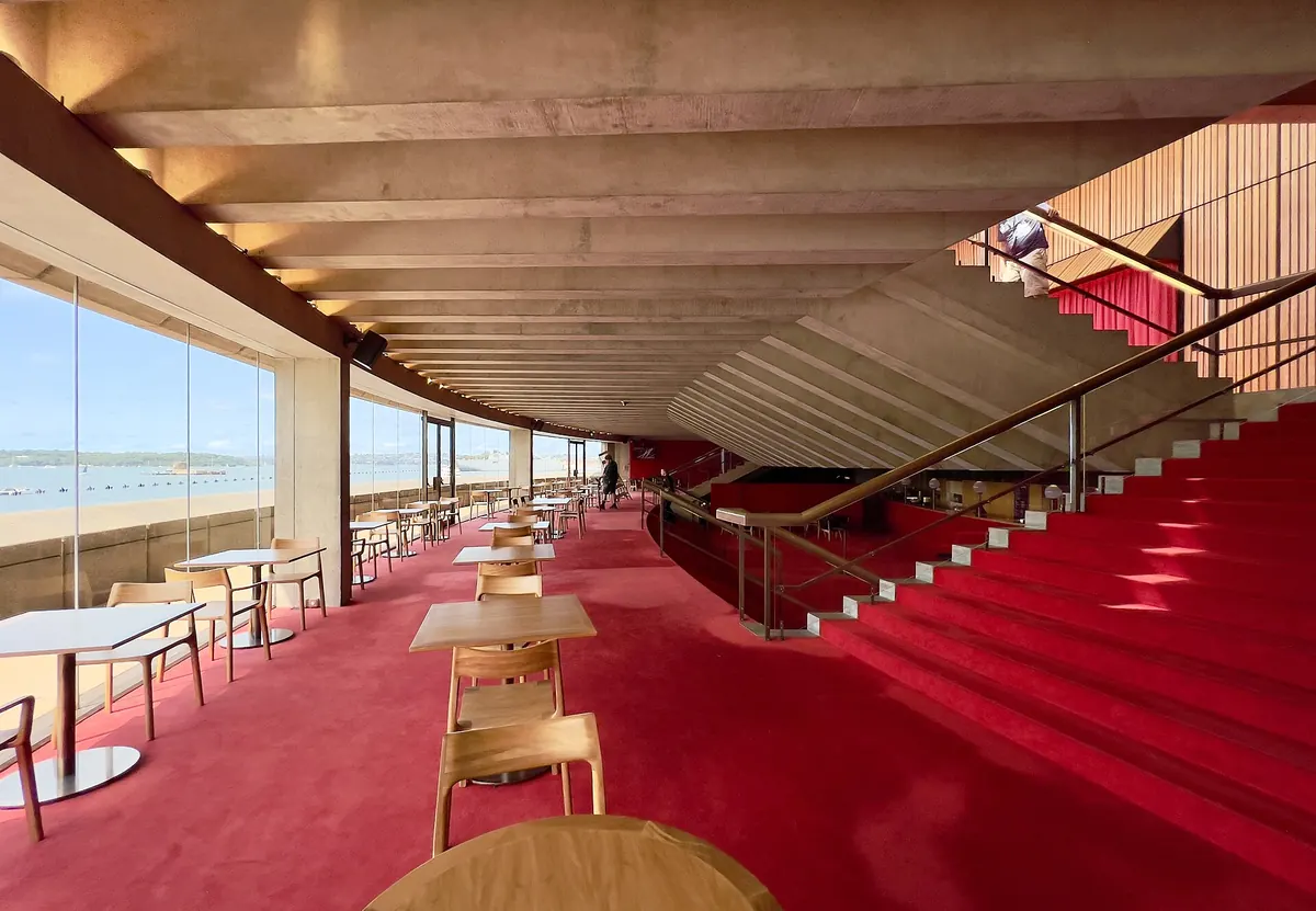 A foyer of the Joan Sutherland Theatre with red carpet, a ribbed concrete ceiling and tall windows over the harbour