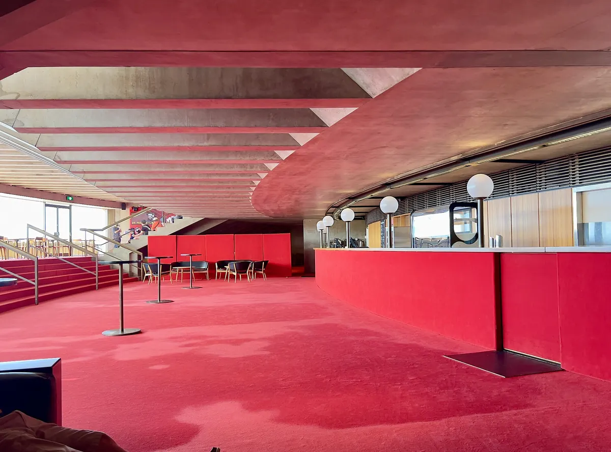 A bar and seating area in a foyer of the Joan Sutherland Theatre, with red carpet and walls and round white lamps